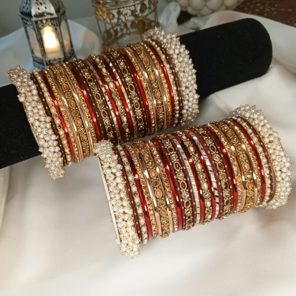 From our Exclusive Collection, this red and maroon bangle set is designed to create an ethereal bridal statement. It features a rich combination of dotted metal bangles in deep maroon, glossy red bangles, and intricate rice work kary in white, maroon, and champagne shades. The look is beautifully finished with luxurious shahi gajray on both ends for a complete royal touch.Perfect for bridal wear, engagement, festive occasions, and traditional events. Deep red and maroon colour palette • Dotted metal bangles • Glossy red finish bangles • Intricate rice work kary • White, maroon, and champagne detailing • Shahi gajray finishing Material Details Bangles: High-quality brass alloy Kary work: Copper alloy Stones & embellishments: Non-precious, premium quality materials Durable, lightweight, and crafted for elegant long wear.