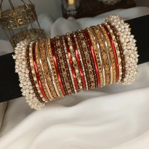From our Exclusive Collection, this red and maroon bangle set is designed to create an ethereal bridal statement. It features a rich combination of dotted metal bangles in deep maroon, glossy red bangles, and intricate rice work kary in white, maroon, and champagne shades. The look is beautifully finished with luxurious shahi gajray on both ends for a complete royal touch.Perfect for bridal wear, engagement, festive occasions, and traditional events. Deep red and maroon colour palette • Dotted metal bangles • Glossy red finish bangles • Intricate rice work kary • White, maroon, and champagne detailing • Shahi gajray finishing Material Details Bangles: High-quality brass alloy Kary work: Copper alloy Stones & embellishments: Non-precious, premium quality materials Durable, lightweight, and crafted for elegant long wear.