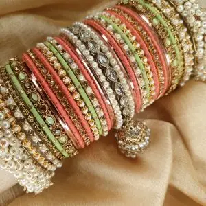 Gulabi is an exclusive handcrafted bangle set featuring a soft blend of mint green, blush pink, and champagne tones. Designed with intricate kundan kary, pearl detailing, teardrop stone accents, and a statement jhumki charm, this set is beautifully finished with luxurious shahi gajray on both ends for a complete bridal look.Perfect for nikkah, engagement, mehndi, walima, and festive occasions. Base Bangles: High-quality brass alloy Kary Work: Copper alloy Stones & Pearls: Non-precious, premium quality stones and artificial pearls Durable, lightweight, and crafted for comfortable long wear.
