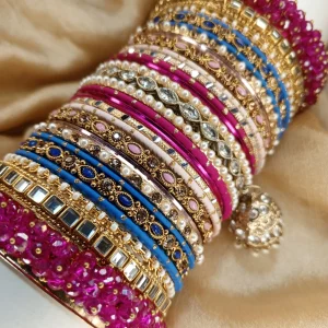 Chamkeli is a vibrant handcrafted bangle set featuring intricate rice work kary in pink and royal blue tones tear dep kundun jhumki The stack is beautifully balanced with detailed stone embellishments and finished with bold magenta gajra on both ends for a rich, statement bridal look. Perfect for mehndi, baraat, engagement, and festive celebrations where colour and elegance come together.
