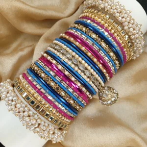 Zarmina is a bold and regal handcrafted bangle set featuring a striking blend of royal blue and magenta tones with champagne gold accents. Designed with intricate stone work, detailed kundan kary, pearl embellishments, and a statement jhumki charm, this set is completed with luxurious shahi pearl gajray on both ends for a full royal bridal finish. Perfect for mehndi, baraat, engagement, and grand festive celebrations.