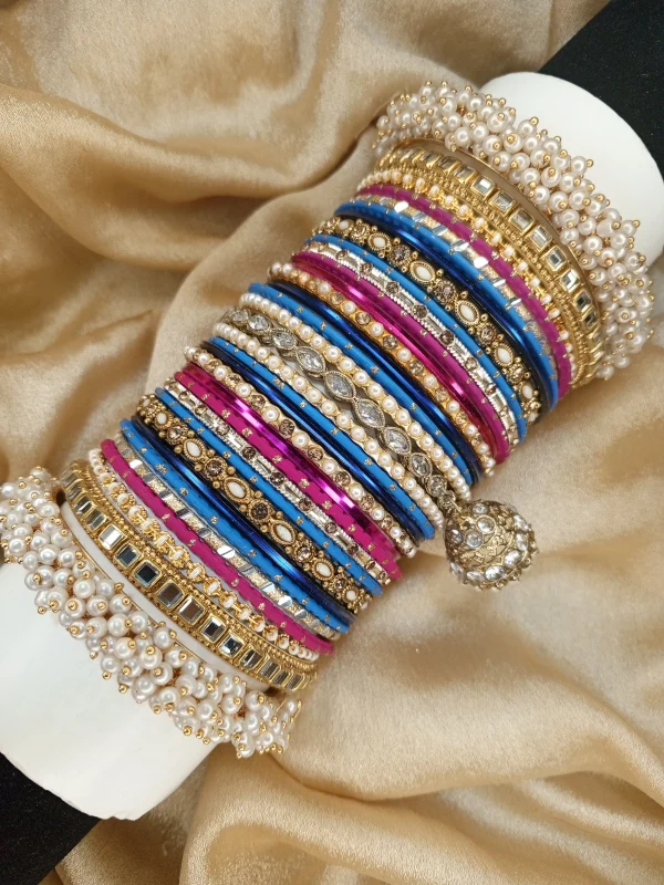 Zarmina is a bold and regal handcrafted bangle set featuring a striking blend of royal blue and magenta tones with champagne gold accents. Designed with intricate stone work, detailed kundan kary, pearl embellishments, and a statement jhumki charm, this set is completed with luxurious shahi pearl gajray on both ends for a full royal bridal finish. Perfect for mehndi, baraat, engagement, and grand festive celebrations.