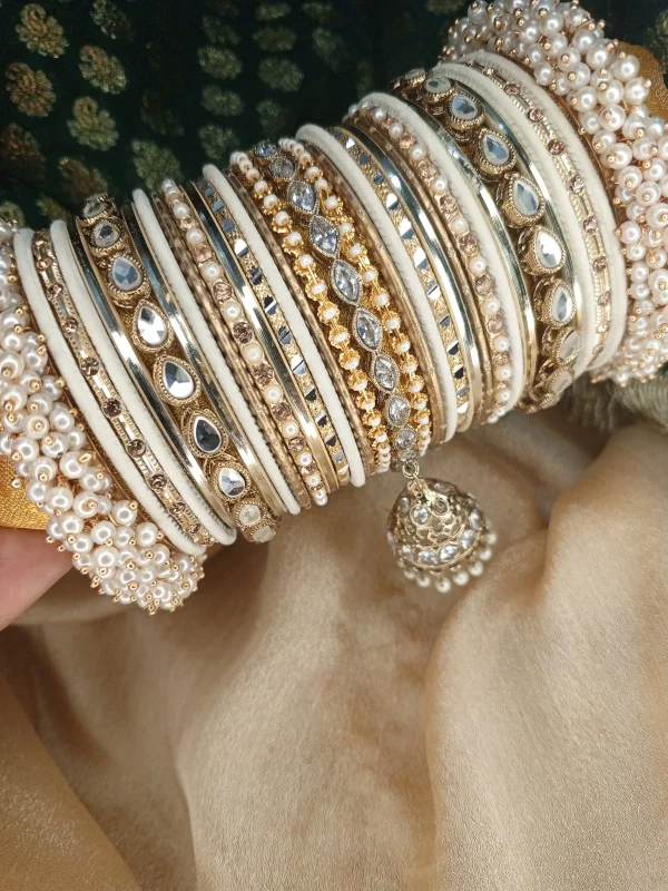 Hoor is a handcrafted white and gold bridal bangle set featuring intricate kundan kary, elegant teardrop stone detailing, a statement teardrop jhumki charm, and sahi pearl gajray on both ends. Perfect for bridal, nikkah, walima, and festive wear. • White and gold classic combination • Detailed kundan kary work • Teardrop crystal stones • Attached jhumki charm • Sahi pearl gajray finish