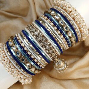 Exclusive Festive Metal Bangle Set Elegant, regal, and effortlessly eye-catching, Neel Aura is a luxurious combination of royal blue, ice blue, pearl white, silver, and antique gold. Designed with sparkling mirror-cut bangles, intricate stone detailing, delicate pearl accents, and beautifully crafted statement centerpiece bangles, this set brings together classic tradition and refined modern elegance. Finished with signature pearl-edge bangles and a graceful jhumki charm, Neel Aura is the perfect choice for mehndi, nikkah, engagement celebrations, Eid, weddings, and formal festive occasions. Whether paired with deep blue, silver, white, or pastel ensembles, it adds a sophisticated sparkle that completes your celebration look. Fully customizable in any color of your choice.