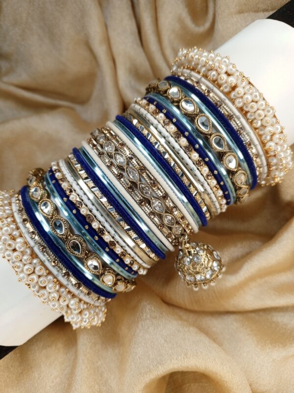 Exclusive Festive Metal Bangle Set Elegant, regal, and effortlessly eye-catching, Neel Aura is a luxurious combination of royal blue, ice blue, pearl white, silver, and antique gold. Designed with sparkling mirror-cut bangles, intricate stone detailing, delicate pearl accents, and beautifully crafted statement centerpiece bangles, this set brings together classic tradition and refined modern elegance. Finished with signature pearl-edge bangles and a graceful jhumki charm, Neel Aura is the perfect choice for mehndi, nikkah, engagement celebrations, Eid, weddings, and formal festive occasions. Whether paired with deep blue, silver, white, or pastel ensembles, it adds a sophisticated sparkle that completes your celebration look. Fully customizable in any color of your choice.